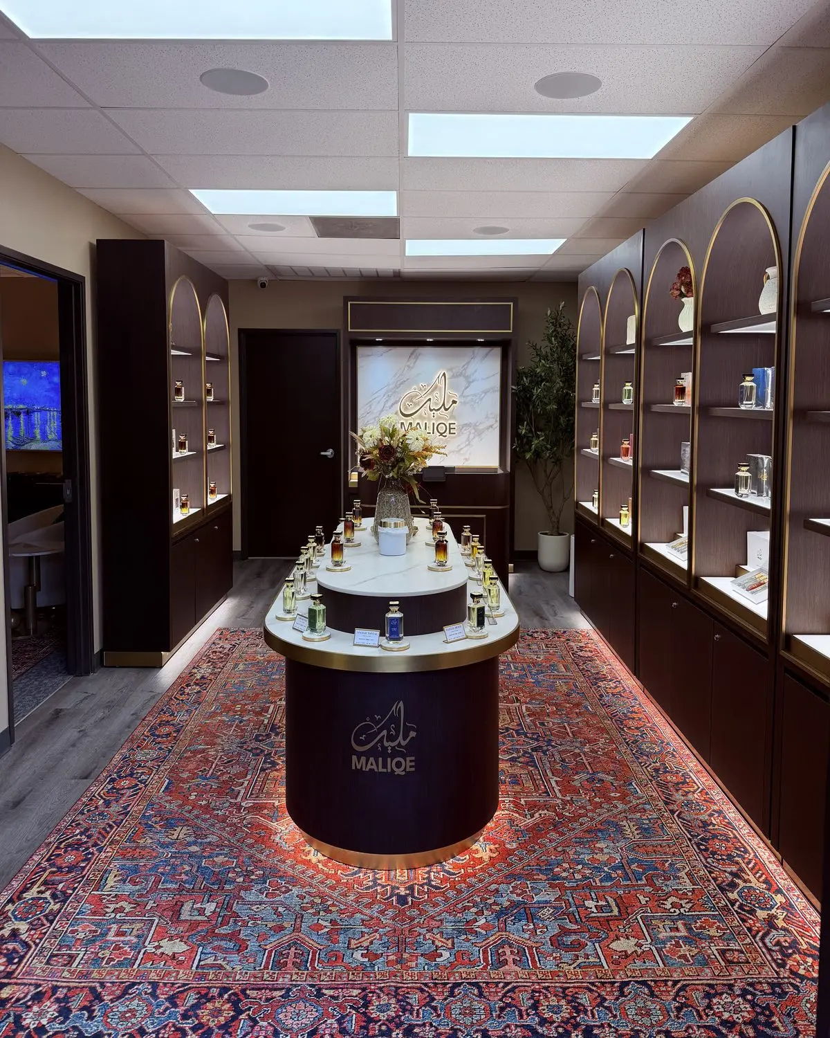 Inside the Maliqe boutique: arched, lit shelving of fragrances and a central MALIQE display on a Persian rug